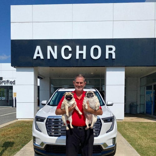 A man holding two pugs, with an Anchor sign visible in the background.